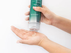 Volumizing shampoo bottle held in hands, green tube with white cap