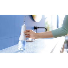 Cordless power flosser held near sink faucet, with clear water reservoir