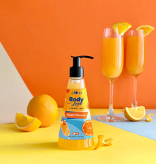Pump-top shower gel bottle on tabletop with citrus fruit and mimosa cups
