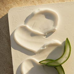 Aloe vera moisturizing cream swirls on skin, creamy pale texture with aloe slices