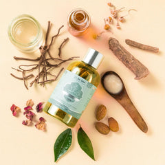 Baby massage oil bottle with silver cap beside open jar and herb stems