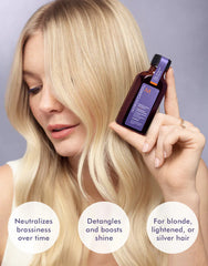 Purple hair treatment bottle in hand beside blonde hair on model, label visible