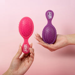 Mini detangling hair brushes, pink and purple, held in hands