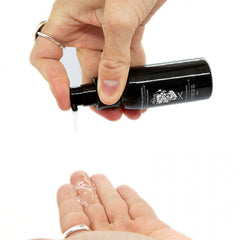 Hand pouring clear serum into palm from black bottle with nozzle