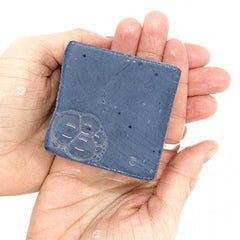 Blue charcoal soap bar square, held in hand, visible bubbles and speckles