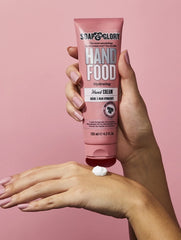 Hydrating hand cream tube in pink held above hands with cream dollop