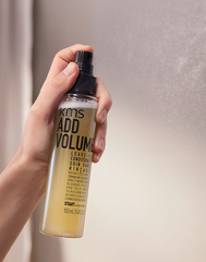 KMS Add Volume leave-in conditioner bottle held in hand, 150 ml, black cap and pale yellow