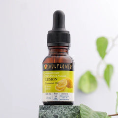 Lemon essential oil bottle with black dropper on stone and greenery.