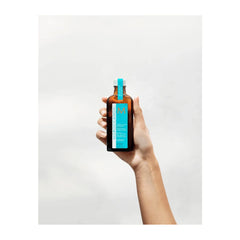 Moroccanoil Treatment Light bottle held in hand, teal label