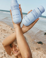 Nak Hydrate Shampoo and Hydrate Conditioner bottles held in hands, light blue