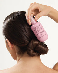 Woman applying NAK Nourish Hair Oil from pink bottle to sleek hair