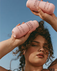 Hand holding pink nourish shampoo and conditioner bottles