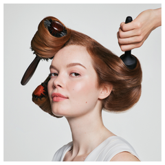 Spray nozzle misting brown hair while a hand twists a section during styling.