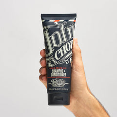 Hair and beard shampoo+conditioner tube held in hand, dark front label with logo
