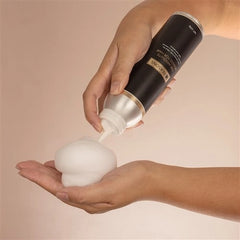 Hair mousse foam dispensed into hands from a black bottle