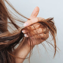 Hair repair balm being smoothed into brown hair strands by hand