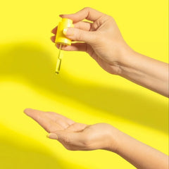 Hand holding yellow dispenser for hair oil, with droplets visible