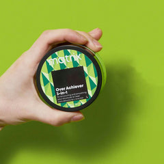 Matrix Over Achiever 3-in-1 hair styling cream jar held in a hand, green label