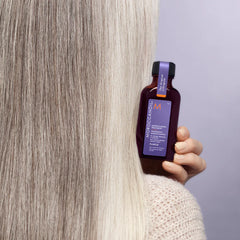 Moroccanoil Purple Treatment bottle held near blonde hair