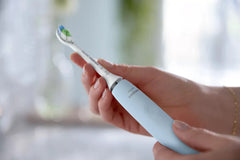 Light blue Philips Sonicare electric toothbrush held in hand, brush head up