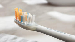 Toothbrush head close-up with orange and blue bristle tufts on white Philips Sonicare handle
