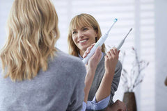 Woman holding Philips Sonicare electric toothbrush, white with teal bristles