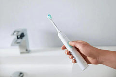 Electric toothbrush held toward camera, white handle and teal bristles