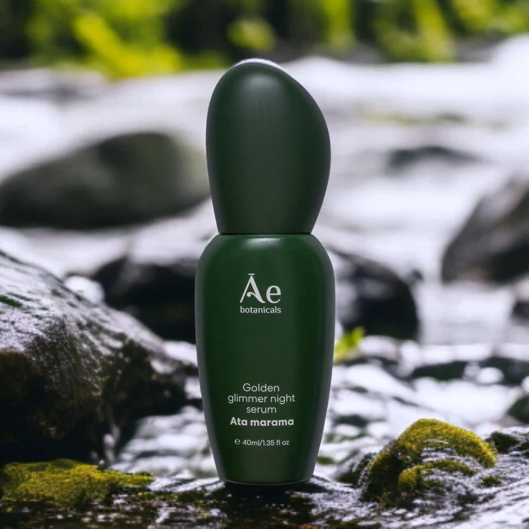 Green night serum bottle on rocks with moss, Ae botanicals label
