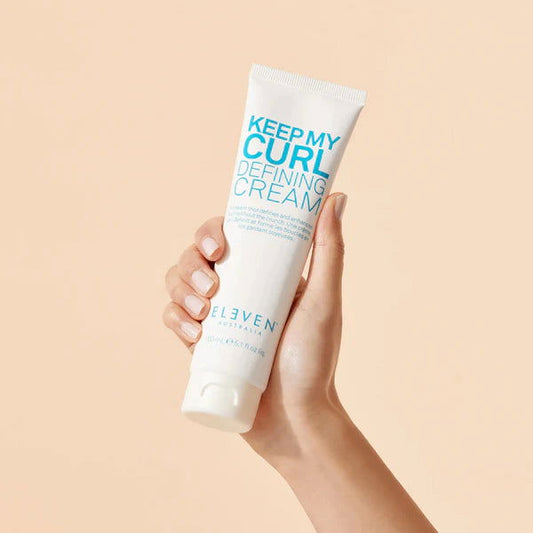 Curl defining cream tube held by hand, 150ml, white with teal Eleven branding