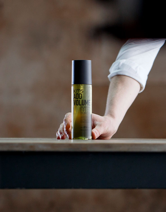 KMS Add Volume volumizing spray bottle in hand, black cap, yellow-green label