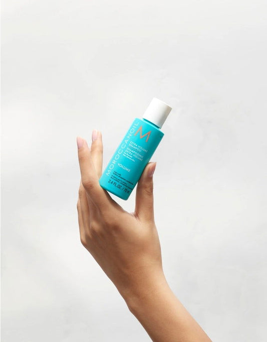 Moroccanoil extra volume shampoo bottle held in hand, teal with white cap