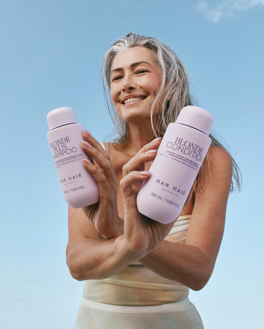 Hair care shampoo and conditioner bottles held by smiling blonde woman