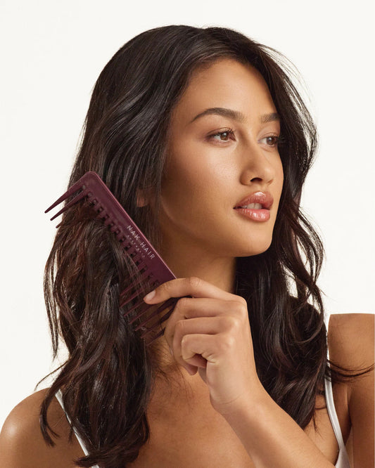 Maroon wide-tooth hair comb held in hands, side view