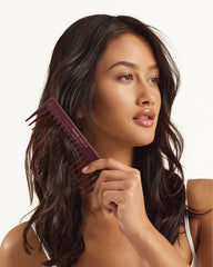 Maroon wide-tooth hair comb held in hands, side view