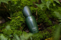 Dark green Ae botanicals serum bottle with rounded cap on green foliage