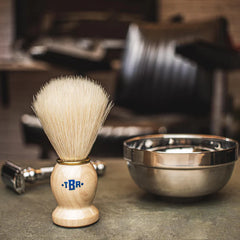 Synthetic shaving brush on countertop with pale bristles and light wood *TBR* handle